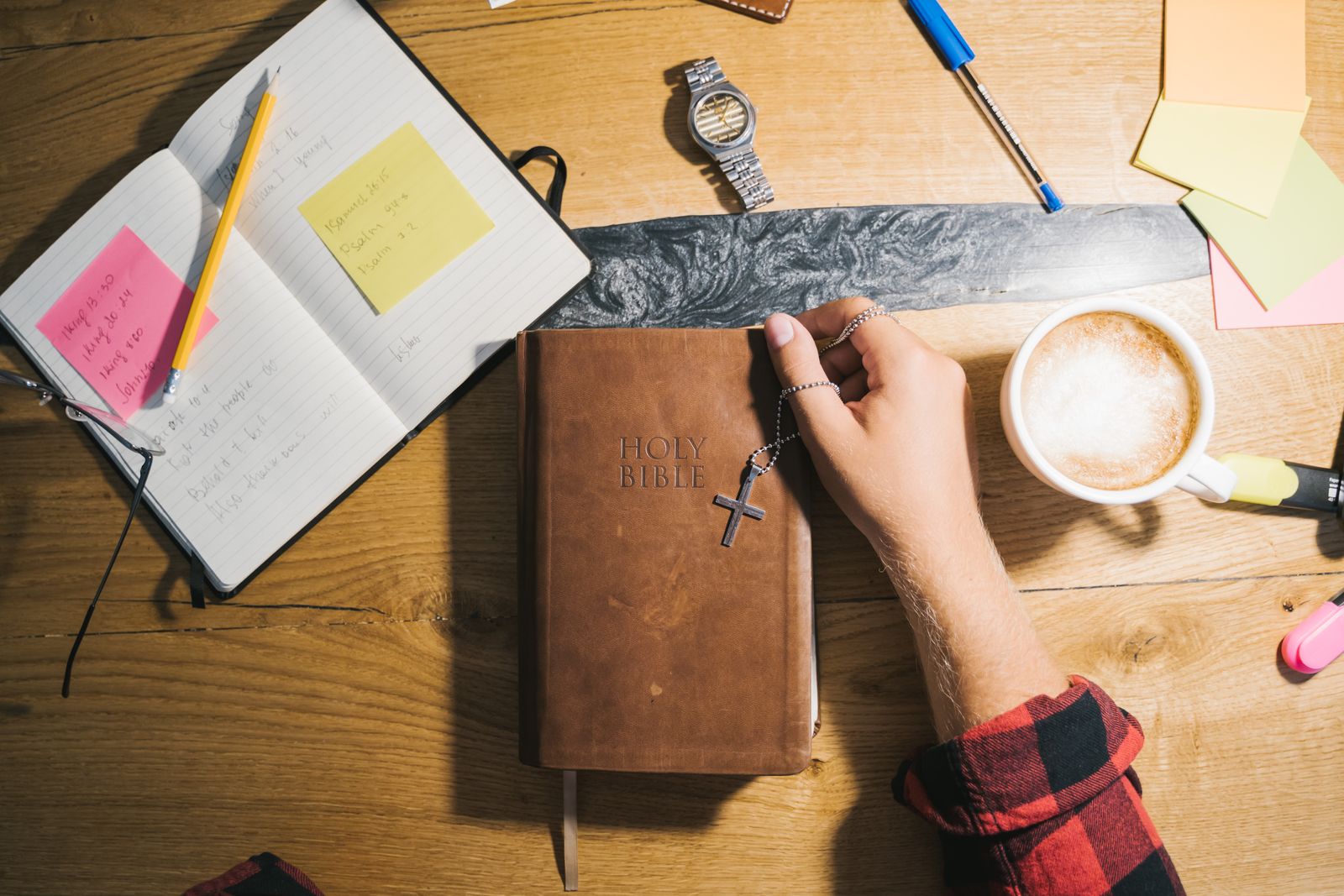 A woman taking prayer journal notes beside an open Bible on a wooden table