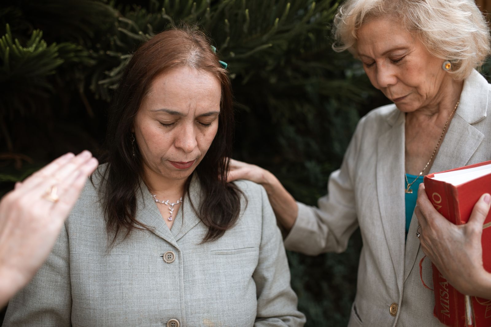 Three women standing together in prayer and supporting one another outdoors